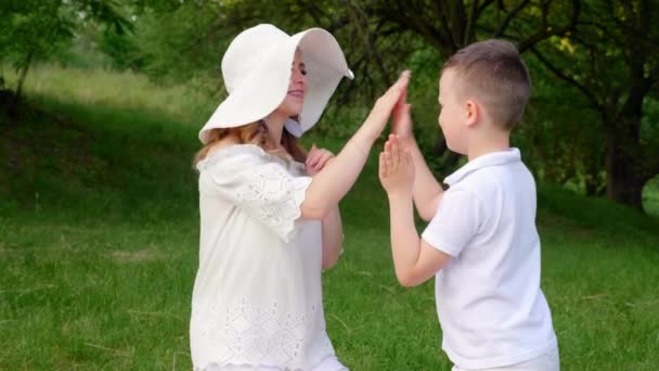 Lycklig mamma i vit hatt och son i t-shirt lek spel i parken på naturen — Stockvideo