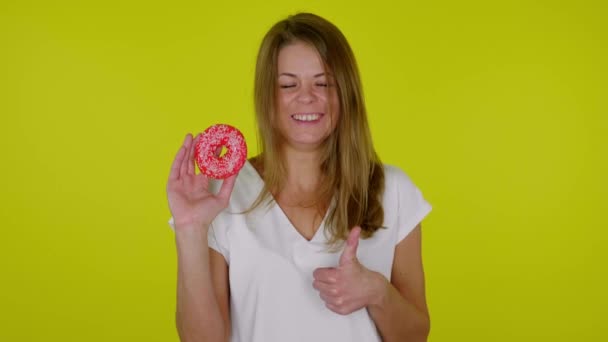 Mujer alegre en una camiseta blanca se ríe con una rosquilla en la mano — Vídeos de Stock