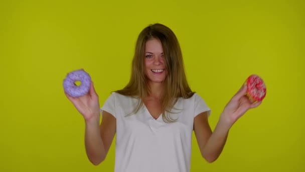 Mulher em uma camiseta branca está dançando com donuts vermelhos e azuis nas mãos, sorrindo — Vídeo de Stock