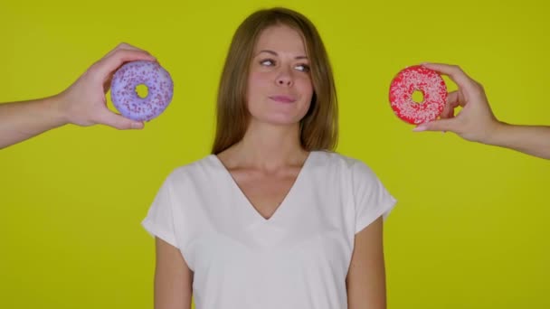 Mulher faminta olha em volta, morde e lambe os lábios e escolhe qual donut comer — Vídeo de Stock