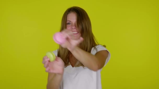 Radosna kobieta tańczy z różowymi i żółtymi makaronikami w dłoniach, uśmiechając się — Wideo stockowe