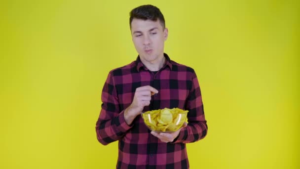Man in een roze geruite shirt eet chips met glazen schaal op gele achtergrond — Stockvideo