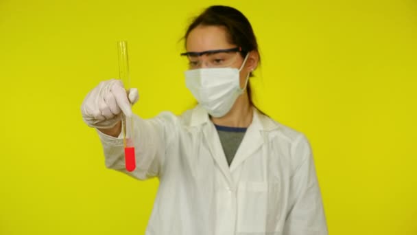 Vrouw in witte medische jurk, beschermend masker is onderzoekt de inhoud van de reageerbuis — Stockvideo