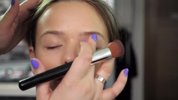 Makeup καλλιτέχνης εφαρμόζει κρέμα ίδρυμα στο πρόσωπο με τα δάχτυλα ενός κοριτσιού στο σαλόνι — Αρχείο Βίντεο