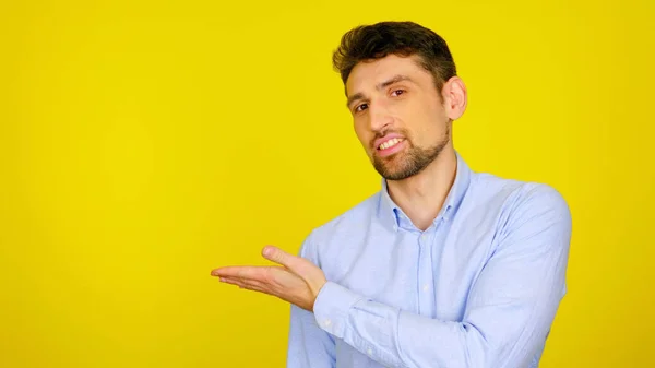 Homem de camisa azul claro sorri e mostra com a mão um lugar para produtos e texto — Fotografia de Stock