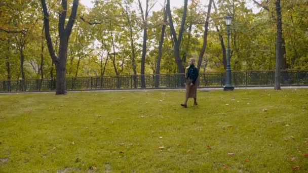 Счастливая женщина черная куртка, леопардовая юбка гуляет по парку, кружится от счастья — стоковое видео