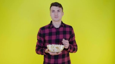 Adam cam kaseden patlamış mısır yiyor, sarı arka plandaki tattan memnun değil.