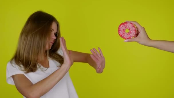 Woman on diet in white T-shirt refuses sweet tasty donut on a yellow background — Stock Video