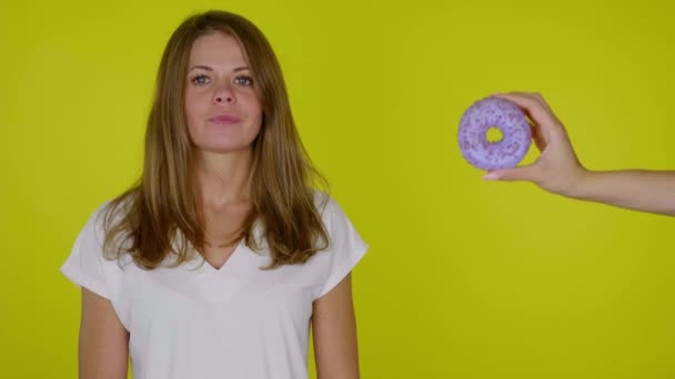 Hungrig kvinna på en diet i en vit t-shirt vill bita munk men det fungerar inte — Stockvideo
