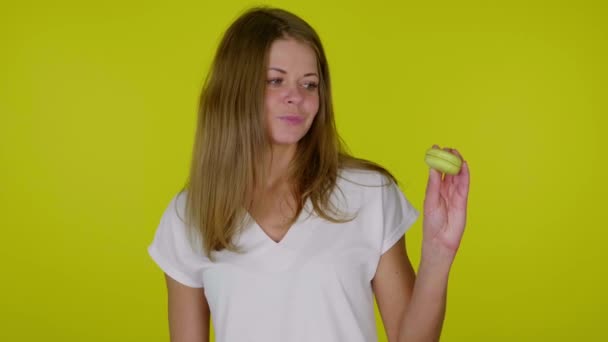 Kvinna i vit t-shirt lyfter handen med en gul makaron, visar som, leenden — Stockvideo