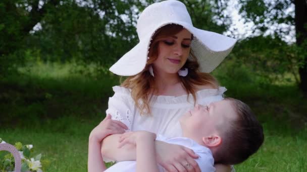 Šťastná máma a syn objímají. Žena a malý chlapec sedí na trávě v parku — Stock video