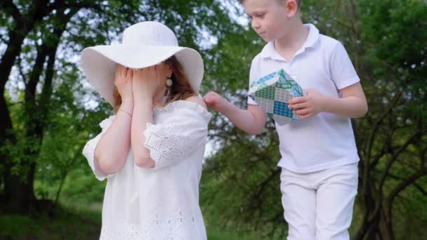 Hijo en pantalones blancos y camiseta le da a mamá en una caja de sombrero blanco con regalo, abrazos — Vídeos de Stock
