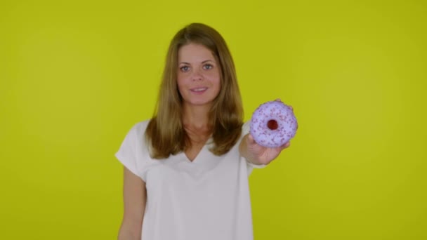 Vrouw in een wit T-shirt steekt de hand op met een blauwe donuts in de camera, glimlacht — Stockvideo