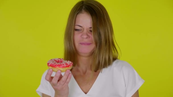 Femme dans un T-shirt blanc mange beignets rouges insipides, spectacles bouleversés détestent — Video