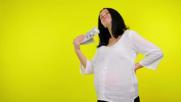 Rik ung gravid kvinna vinkar pengar framför hennes ansikte på gul bakgrund — Stockvideo