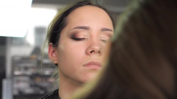 Make-up kunstenaar brengt stichting op een gezicht met borstel naar vrouw in schoonheidssalon — Stockvideo