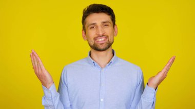 Açık mavi gömlekli yakışıklı sakallı adam elleri havada gülümsüyor.