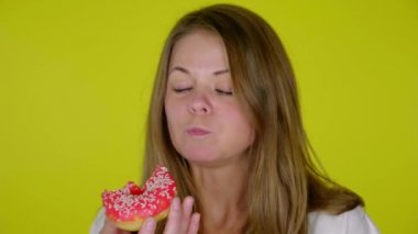 Beyaz tişörtlü aç kadın ısırıyor, lezzetli kırmızı çörekler yiyor.