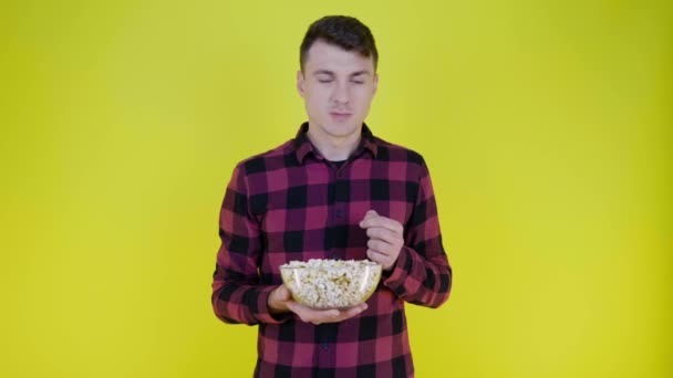 Člověk jí popcorn ze skleněné mísy, nespokojen s chutí na žlutém pozadí — Stock video