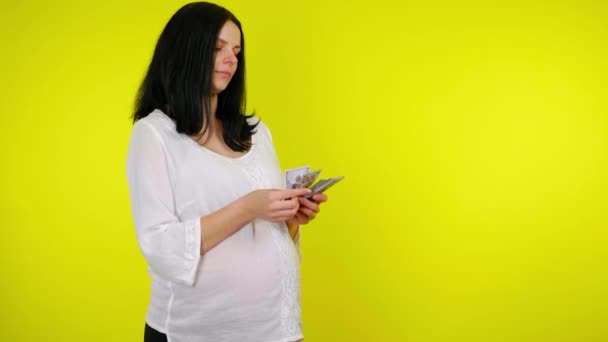 Rik ung gravid kvinna med svart hår räknar pengar på en gul bakgrund — Stockvideo