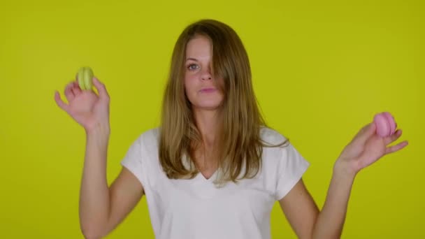Mulher em uma camiseta branca está dançando com macaroons rosa e amarelo nas mãos — Vídeo de Stock