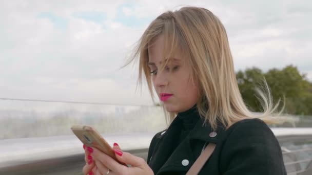 Женщина в черной куртке пользуется смартфоном на улице. Отснятый в замедленном режиме 4К — стоковое видео