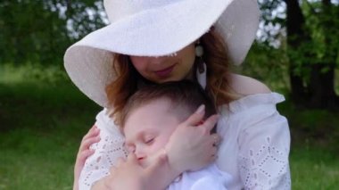 Mutlu anne ve oğul kucaklaşması. Kadın, çocuk parkta çimlerde oturuyor, gülümsüyor.
