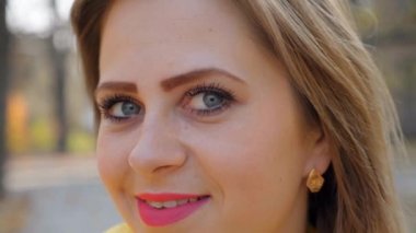 Kadın başını kapat: yüz göz burun dudak. Açık havada pembe rujlu kız gülümsüyor.