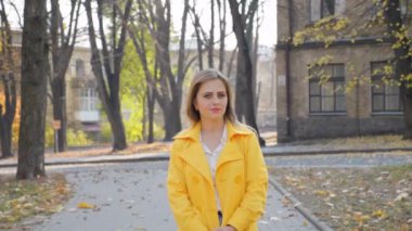 Pelerinli kadın, bluz duruyor, parktaki kameraya bakıyor, kamera kızı hareket ettiriyor.