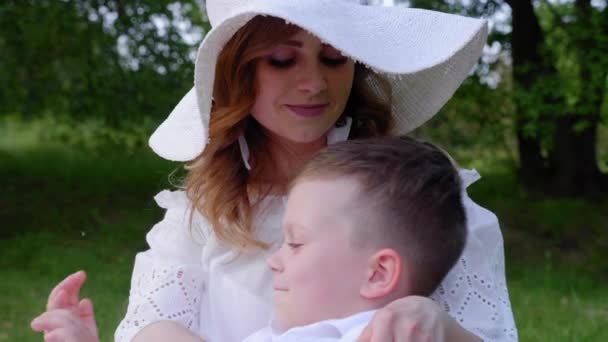 Szczęśliwa mama, przytulanie syna. Kobieta, chłopiec siedzący na trawie w parku, uśmiechnięty — Wideo stockowe