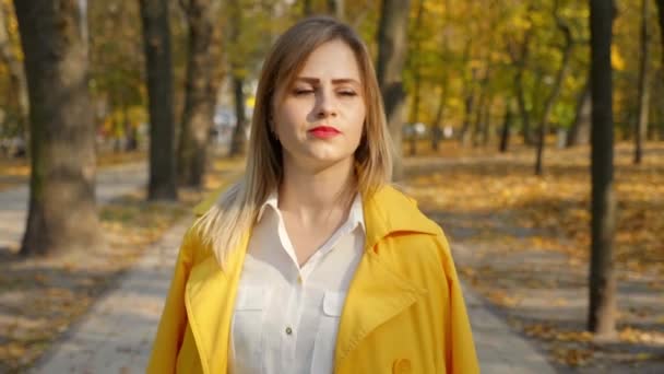Vrouw in gele mantel loopt herfst park, kijkt rond, geniet — Stockvideo