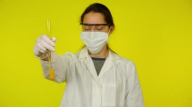 Beyaz elbiseli kadın, koruyucu maske test tüpünün içindekileri inceliyor.