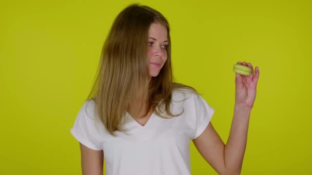 Kvinna i vit T-shirt höjer handen med gul makaron, visar som, leenden — Stockvideo