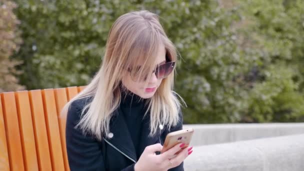 Mujer en gafas de sol termina hablando de teléfono celular, bloquea teléfono inteligente, pone en bolsa — Vídeos de Stock