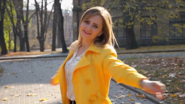 Radostná žena ve žlutém plášti tančící v podzimním parku s úsměvem. Zpomalený pohyb — Stock video