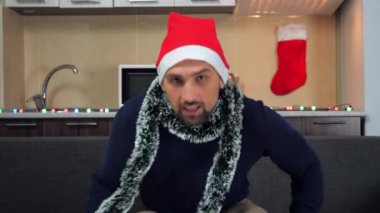 Yeni yılda pozitif adam kırmızı Noel Baba şapkası televizyon izler, gülümser.