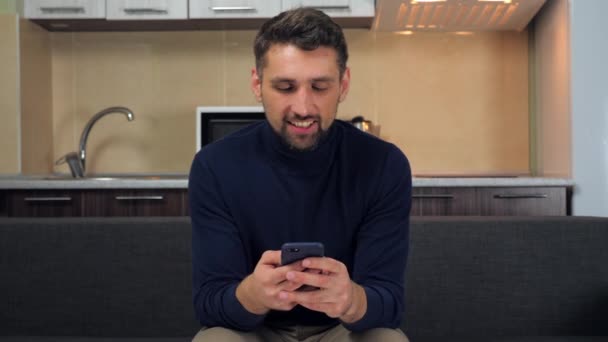 Homem bonito alegre sorrindo usa mensagem de digitação de smartphone no messenger — Vídeo de Stock