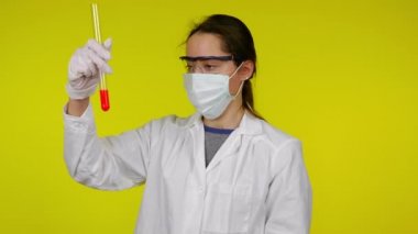 Koruyucu maskeli kadın test tüpünün içeriğini inceliyor ve hoşlanmadığını gösteriyor.