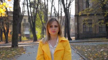 Kadın pelerinli, bluz parkta duruyor, kamera kızı çekiyor.