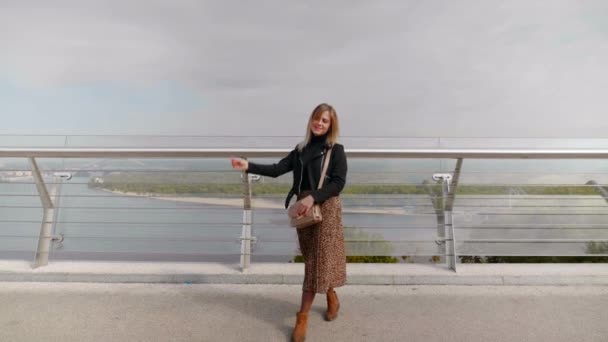 前向きな女性が背景の橋の上にポーズをとって笑っています — ストック動画