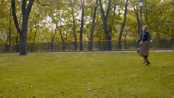 Счастливая женщина черная куртка, леопардовая юбка гуляет по парку, кружится от счастья — стоковое видео