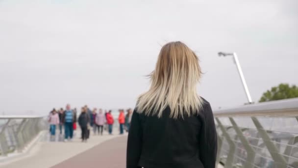 Baksidan kvinna i svart jacka promenader fotgängare bro, ser sig omkring utomhus — Stockvideo