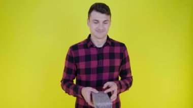 Pembe ekose gömlekli yakışıklı adam hediye kutusunu elden ele, sarı arka planda fotokopi alanı ile fırlatıyor. Metin ya da ürün için yer. 4K yavaş çekim görüntüleri