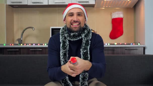 Positive man in New Year red Santa Claus hat, explodes confetti cannon, smiles — Stock Video