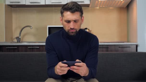 Känslomässig manlig spelare spelar TV-spel på smartphone, förlorar, missnöjda resultat — Stockvideo