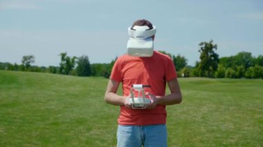Adam uzaktan kumandayla dronu kontrol ediyor, kafasında gözlüklerle videoya bakıyor.