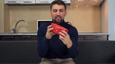 Mutlu yakışıklı adam kırmızı kutuyu inceler, öpücükler, sarılmalar, hediyeler ve gülümsemeler.