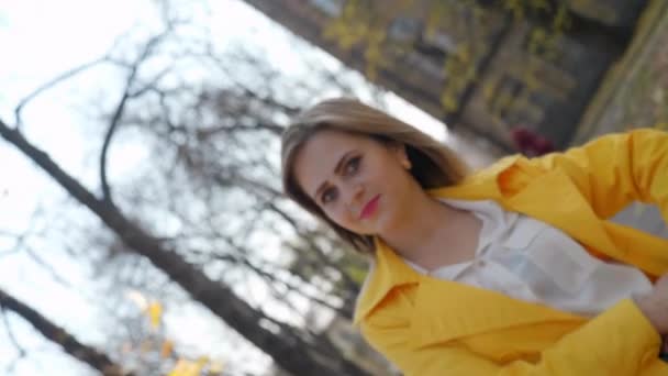 Femme en manteau jaune, chemisier sourit, se tient parc d'automne, regarde caméra tourne — Video