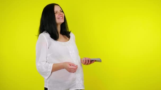 Беременная женщина стоит с кучей денег в руке смеясь и разговаривая — стоковое видео