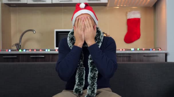 Шокированный человек в новогодней красной шляпе Санта-Клауса смотрит телевизор закрывает лицо руки — стоковое видео